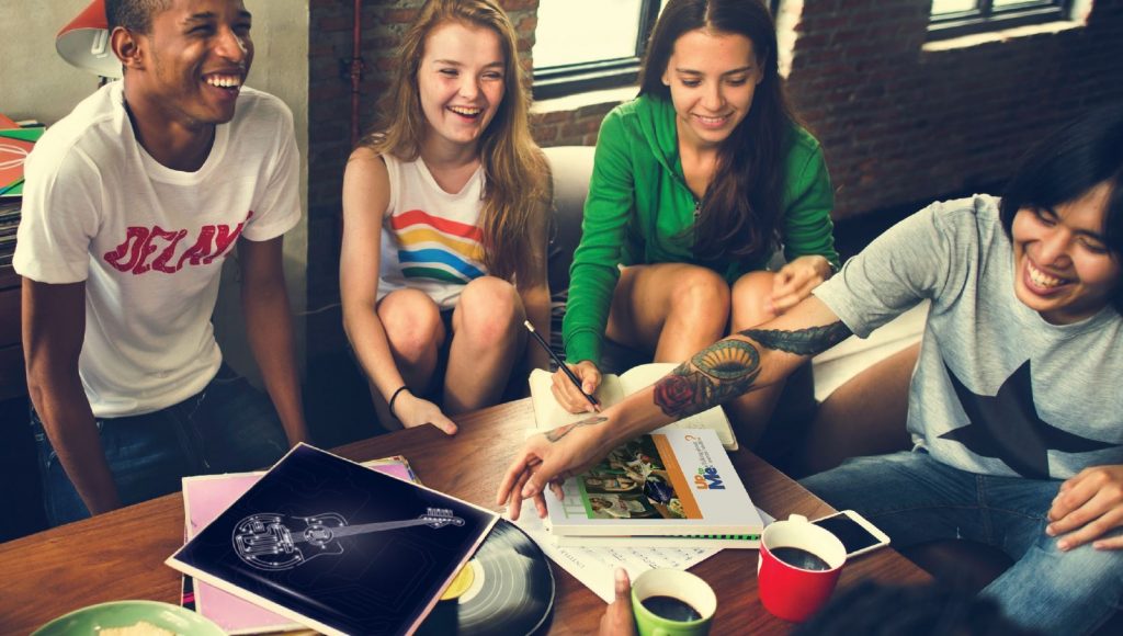 A group of 4 teenagers in a casual setting in a conversation, laughing and smiling.